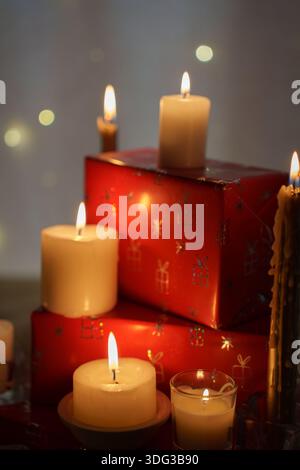 Warmes Urlaubsambiente mit leuchtenden Kerzen und festlicher Einrichtung in sanftem Licht, roten Geschenkboxen und sanften Kerzenflammen, die eine gemütliche, ruhige Atmosphäre schaffen Stockfoto