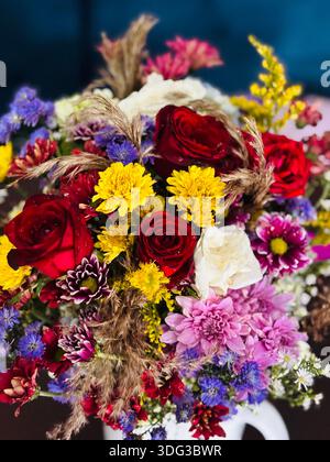 Farbenfrohe Blumenstrauß mit roten Rosen, Chrysanthemen und Wildblumen in dekorativer Blumendekoration. Frische Blütenblätter mit sichtbarem Wasser Stockfoto
