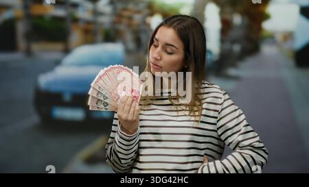 Frau, die isländische Krone draußen hält, mit einem nachdenklichen Ausdruck auf einem Stadtstraßenhintergrund. Stockfoto