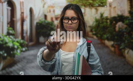 Frau zeigt den Finger in der Straße nach vorne, hält Notizbücher und Rucksack, während sie Brille und Jeansshirt trägt; Bestimmungsgrenze. Stockfoto