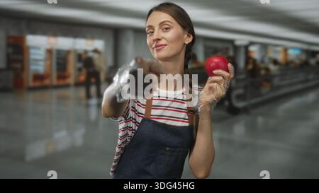 Frau, die roten Apfel hält, mit Handschuhen und Finger darauf im Flughafenterminal zeigt; frischer Snack fröhlich. Stockfoto