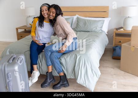 Verschiedene Eltern und Teenager-Tochter umarmen sich auf dem Bett mit grauer Bettdecke im Schlafzimmer mit Koffer und Kisten Stockfoto