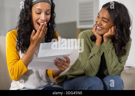 Diverse Mutter und Teenager-Tochter reagieren auf gefalteten Brief auf der Couch im Wohnzimmer Stockfoto