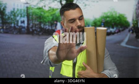Mann mit gerollten Blaupausen hebt die Hand für Stoppgeste auf der von Fahrrädern gesäumten Stadtstraße; Warnung. Stockfoto