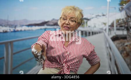 Frau streckt die rechte Hand für Handshake mit Armbändern und Brillen auf einem Straßenpier am Yachthafen, lächelt und begrüßt die Kamera; warme Welcom Stockfoto