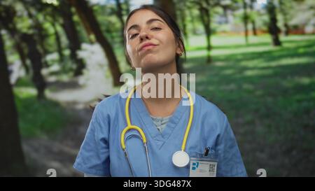 Junge hispanische Ärztin mit Stethoskop in einer Parkumgebung, trägt eine Uniform, vermittelt ein Outdoor-Gesundheitsthema mit Natur Hintergrund. Stockfoto