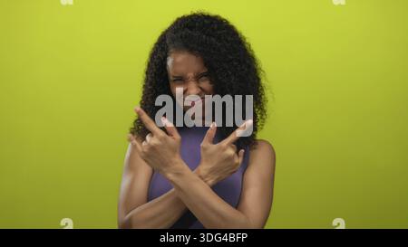 Eine junge Frau mit lockigen Haaren und erhobenen Armen zeigt Gesten mit Steinhörnern in einem gelben Studio-Setting; lustige Stimmung. Stockfoto