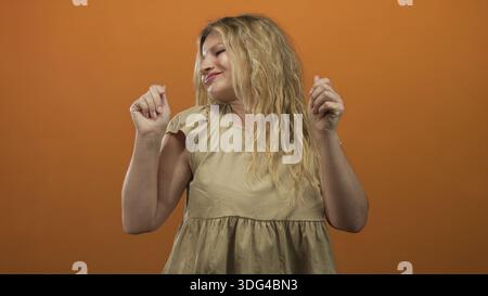 Frau tanzt mit erhobenen Händen und ausdrucksstarkem Gesicht in einem Atelier mit orangenem Hintergrund; Joyrhythmusbewegung. Stockfoto