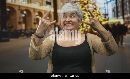 Frau Senior mit Tanktop und Strickjacke, die Steinhandgeste mit Händen und Lächeln im Bauen zeigt; spielerisches Selbstvertrauen. Stockfoto