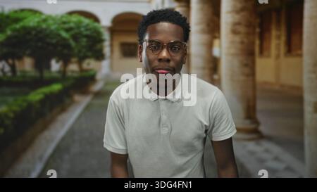 Mann in weißem Poloshirt mit Brillengesten mit erhobener Hand im Gebäude; Selbstvertrauen fokussieren Optimismus stärken. Stockfoto