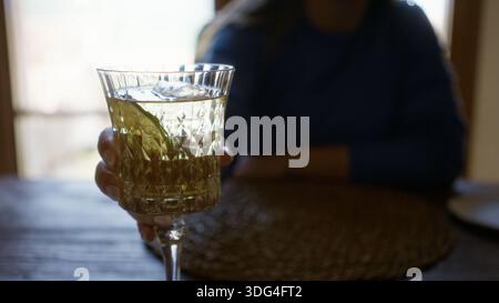Frau genießt Wermut in einem mediterranen Restaurant, hält ein dekoratives Glas drinnen, zeigt eine junge hispanische schöne Szene mit einer entspannten Stockfoto