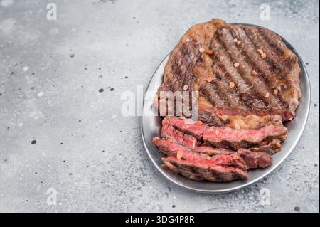 Mittelseltenes Ribeye-Steak in Scheiben geschnitten und mit grobem Salz abgeschmeckt. Gegrilltes Rib Eye Beef auf ovaler Schale mit sauberem Kopierraum Stockfoto