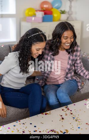 Diverse Mutter und Teenager-Tochter sitzen auf Sofa im Wohnzimmer mit Konfetti, Geschenkboxen Stockfoto