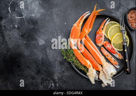 Luxuriöse kamtschatka-Krabbenbeine mit Zitronenscheiben und frischen Kräutern auf dunklem Teller Gourmet-Meeresfrüchte auf strukturiertem schwarzem Hintergrund. Stockfoto