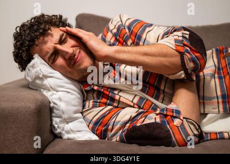 Gestresster junger Mann, der Kopfschmerzen hat, während er zu Hause auf dem Sofa liegt. Stockfoto