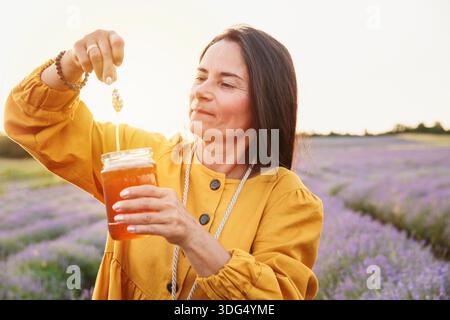 Frau, die Lavendelblume mit tropfendem Honig auf dem Feld hebt Stockfoto