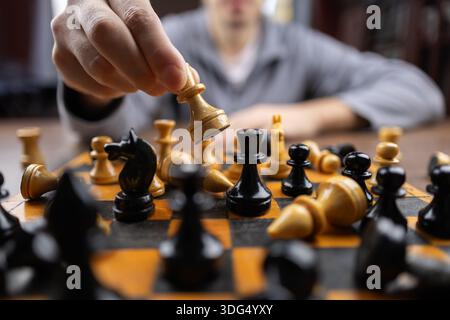 Nahaufnahme des sich bewegenden Schachspiels auf dem Schachbrett, während er am Tisch sitzt. Person, die mit Freunden Strategie-Brettspiel spielt, während sie zu Hause in der Seele sitzt Stockfoto
