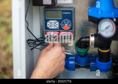 Eine Nahaufnahme der Hände eines Technikers, die dünne elektrische Drähte mit dem Anschlussblock eines digitalen Bewässerungsschalters verbinden. Russland, Region Krasnodar, April Stockfoto