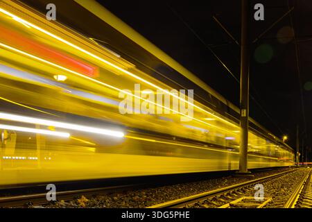 Langbelichtungsaufnahme einer rasanten gelben Straßenbahn, die nachts in Utrecht, Niederlande, leichte Bewegungspfade erzeugt. Stockfoto