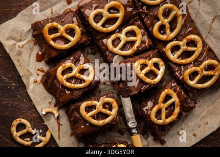 Schokoladen-Brownies mit Nüssen, gesalzenem Karamell und Brezeln, Blick von oben, hölzerner Hintergrund Stockfoto