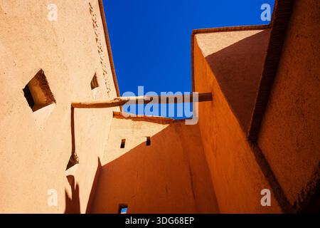 Sonnendurchflutete Lehmbäume mit Holzbalken und Fenstern vor einem klaren blauen Himmel. Ouarzazate, Marokko Stockfoto