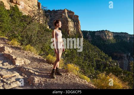 Frau, die auf felsigen Klippen steht, mit Blick auf den bewaldeten Canyon, unter klarem blauem Himmel USA Stockfoto