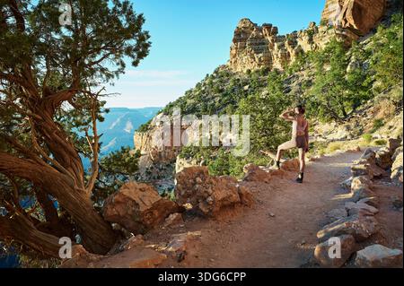Ein Wanderer auf einem felsigen Pfad mit malerischem Blick auf den Canyon und klarem blauem Himmel im Hintergrund. Grand Canyon, Arizona, USA Stockfoto