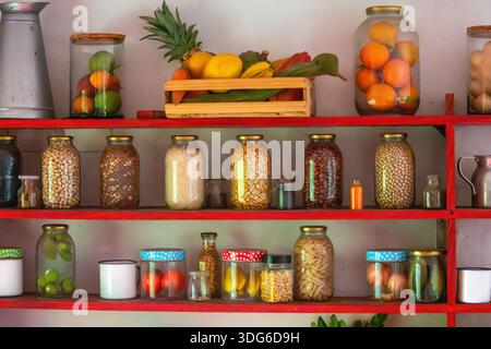 Ein lebhaftes Küchenregal mit Gläsern mit konserviertem Obst, Gemüse und Zutaten, das eine organisierte und farbenfrohe kulinarische Ausstellung präsentiert. Stockfoto