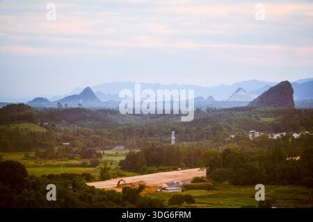 Malerische Aussicht auf üppige grüne Hügel und ferne Berge unter einem bewölkten Himmel. Ausflug von Guilin nach Chengdu, Guangxi, Sichuan, China Stockfoto