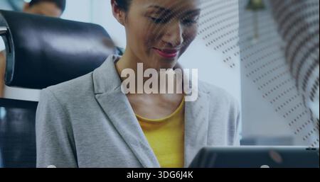 Lächelnde Frau in hellgrauem Blazer und gelbem Top, die Laptop im Büro studiert, Privatsphäre Panel, Stuhl Stockfoto
