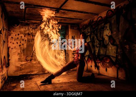 Feuerdarsteller kniend, drehte Feuer-poi in einem mit Graffiti bedeckten Raum nachts. WA, USA Stockfoto