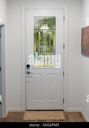 Klare Gestaltung einer Eingangstür mit dekorativer Glasscheibe in einem Flur mit hellem Holzfußboden und Wandbildern Stockfoto