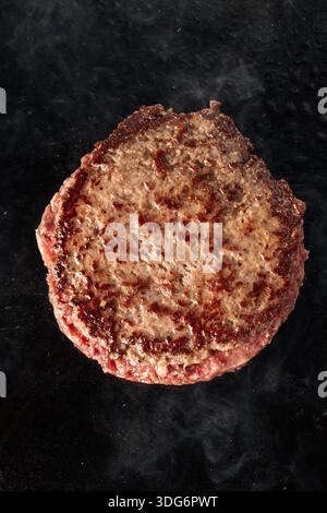 Nahaufnahme von Rindfleisch, das über offenen Flammen gegrillt wird, mit brutzelnder Textur, Saibspuren und aufsteigendem Rauch. Saftiges Fleisch auf einem heißen Grill. Stockfoto