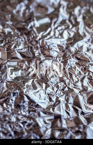 Zerknitterte Aluminiumfolie reflektiert Licht und schafft abstrakte silberne Muster und Texturen Stockfoto