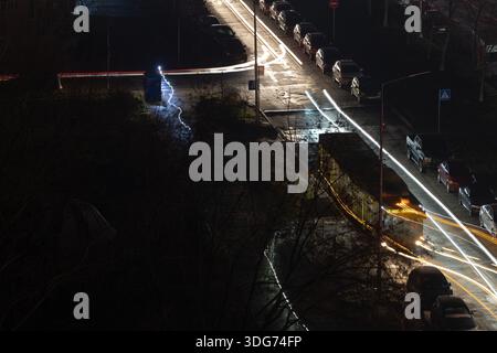 Kiew, Ukraine – 28. November 2024: Öffentliche Verkehrsmittel auf der Revutskoho Street und Autos auf dunkler Straße. Lange Belichtungsdauer von Rot- und Weißlicht. Energieinfrastruktur Stockfoto