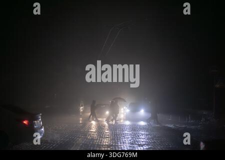 Kiew, Ukraine – 24. November 2022: Silhouetten von Menschen, die eine dunkle, nebelige Straße in der Nähe des Mykhailivska-Platzes überqueren. Autoscheinwerfer bieten das einzige Licht in t Stockfoto