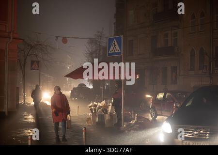 Kiew, Ukraine – 24. November 2022: Silhouetten von Menschen gehen bei einem Winterausfall an einem Blumenhändler in der Jaroslawiv-Val-Straße vorbei. Helle Autoscheinwerfer Stockfoto