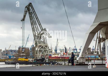 Hamburg Deutschland - 21. Februar 2020. Ein Hafenarbeiter, der auf dem Dock neben dem riesigen Gebäude eines HHLA-Schwimmkrans steht. Industrielle Hafenszene mit Stockfoto
