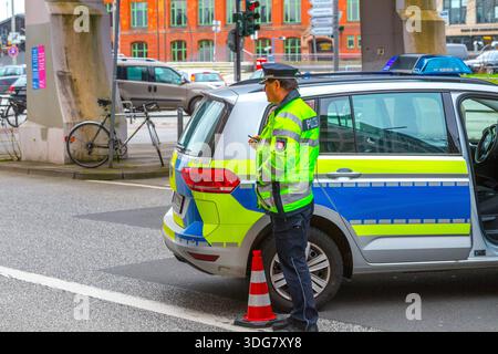 Hamburg, Deutschland – 21. Februar 2020: Polizeibeamter in Warnjacke steht freitags neben dem Streifenwagen in der Nähe der Verkehrskegel-Sperrstraße Stockfoto