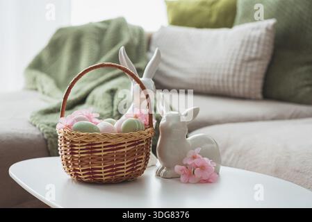 Osterkorb mit Ester-Eiern, Plüschhase und Frühlingsdekor auf weißem Tisch im Cozy Wohnzimmer Stockfoto