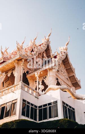 Wat Huay Pla Kang Tempel in Chiang Rai. Februar 2025. Flacher Blick auf eine kunstvoll verzierte weiße Tempeldachecke mit komplizierten Schnitzereien, klarer blauer Himmel/ Stockfoto