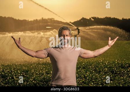 Landwirt steht neben Sprinklern. Wassersprinkler zur Bewässerung des Erntefelds Tropfbewässerungssystem. Bewässerung des Ernteguts. Landwirtschaft und Landwirtschaft. Mann bei Stockfoto