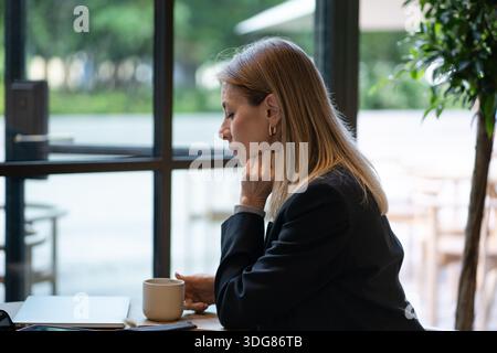 Eine durchdachte Geschäftsfrau denkt über Projekt- und Finanzinformationen nach, während sie einen Kaffee im Café trinkt. Stockfoto