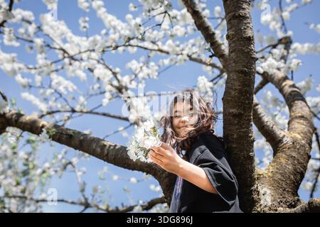 Tiefwinkelansicht eines Mädchens, das Blumen in der Hand hält und gegen blühenden Baum steht Stockfoto