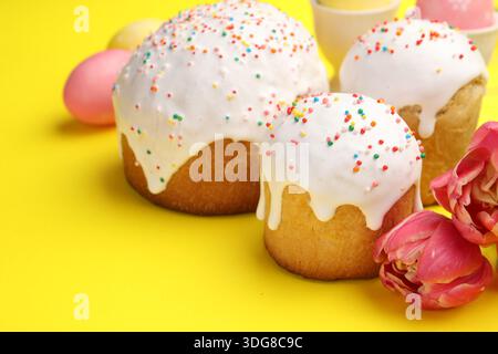 Köstliche Osterkuchen, Eier und Tulpen auf gelbem Hintergrund, Nahaufnahme Stockfoto