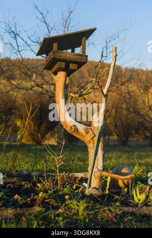 Kleines Vogelhaus auf einem Baumstumpf in einem Garten, umgeben von Pflanzen. Stockfoto