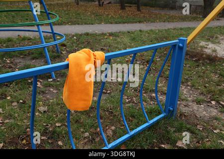 Ein hellorangefarbenes Handtuch hängt an einem blauen Metallgeländer auf einem Spielplatz. Der Boden zeigt gefallene Blätter, was darauf hinweist, dass es sich um einen Fall handelt. Die Gegend ist ruhig und es gibt keine Leute. Stockfoto