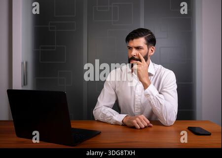 Mann, der in einem modernen Büro sitzt und ein Unternehmen oder ein Unternehmen repräsentiert, das ein weißes Hemd trägt Stockfoto