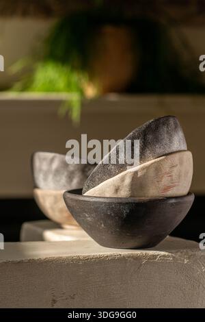 Eine minimalistische Komposition aus handwerklichen Schalen aus Steingut, die auf einem Steinvorsprung angeordnet sind, mit rustikalen Texturen und organischen Glasuren in Anthrazit-Schwarz. Stockfoto