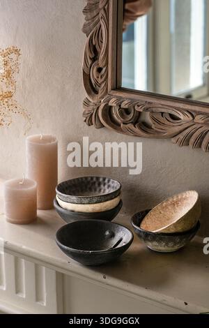 Eine Nahaufnahme einer kuratierten Inneneinrichtung mit einem Stapel handgefertigter, strukturierter Keramikschalen auf einem Kaminsims, neben hohen Kerzen und einem Be Stockfoto